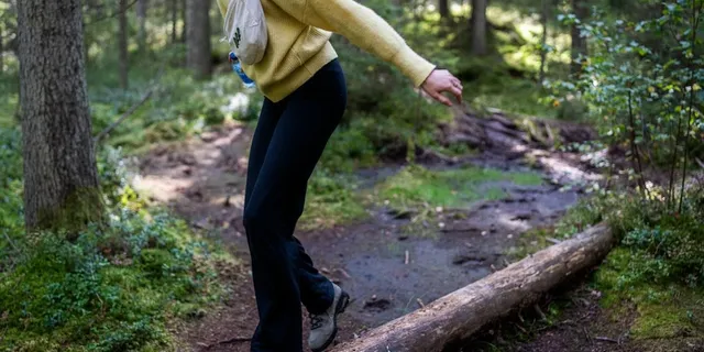 Frau mit Bauchtasche spaziert in Wanderkleidung auf Baumstamm