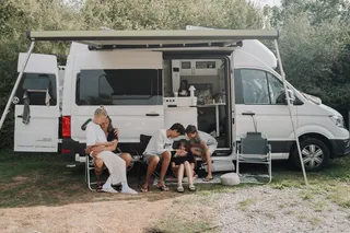 Familie mit Kindern sitzt auf Campingplatz vor ihrem Camper