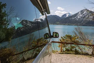 Ein Off Camper vor dem Ufer eines Sees, in dessen Fenster sich das Wasser spiegelt