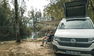 Paar sitzt vor VW T6 an einem See